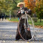 A lady in old-fashioned clothing next to a penny-farthing