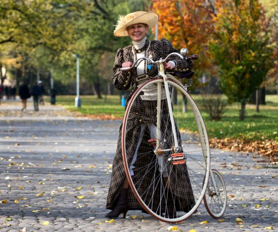 A lady in old-fashioned clothing next to a penny-farthing